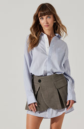 A woman is wearing a light blue, long-sleeved, button-up shirt with vertical white and blue stripes. The shirt has a pocket on the left side of the chest and the sleeves are cuffed at the wrists.